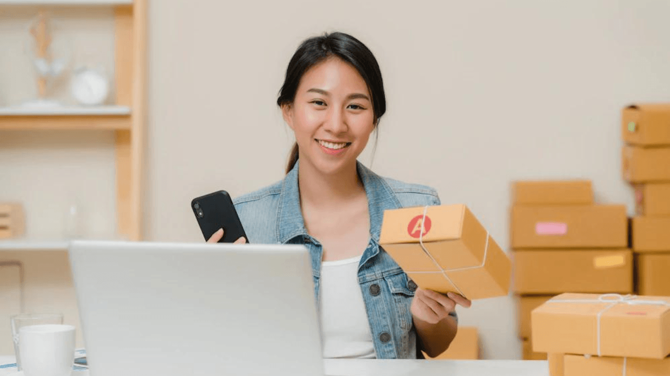 A happy online retailer holding a parcel and a mobile phone