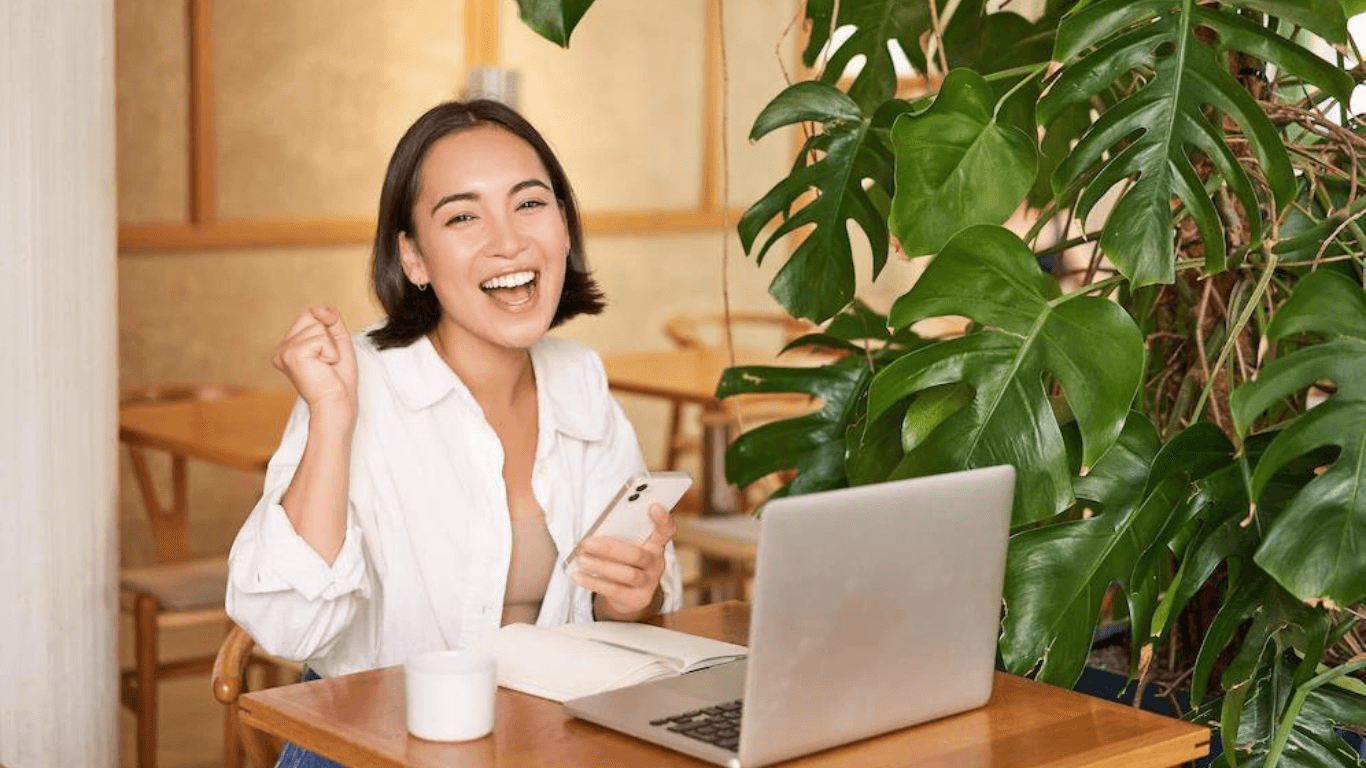 A happy woman celebrating in front of her laptop in a cafe